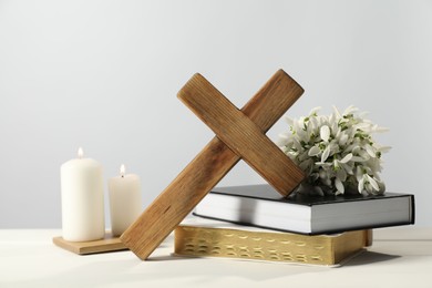 Burning church candles, wooden cross, ecclesiastical books and flowers on white table