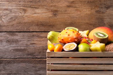 Crate with different exotic fruits on wooden background. Space for text