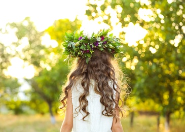 Little girl wearing wreath made of beautiful flowers outdoors on sunny day, back view