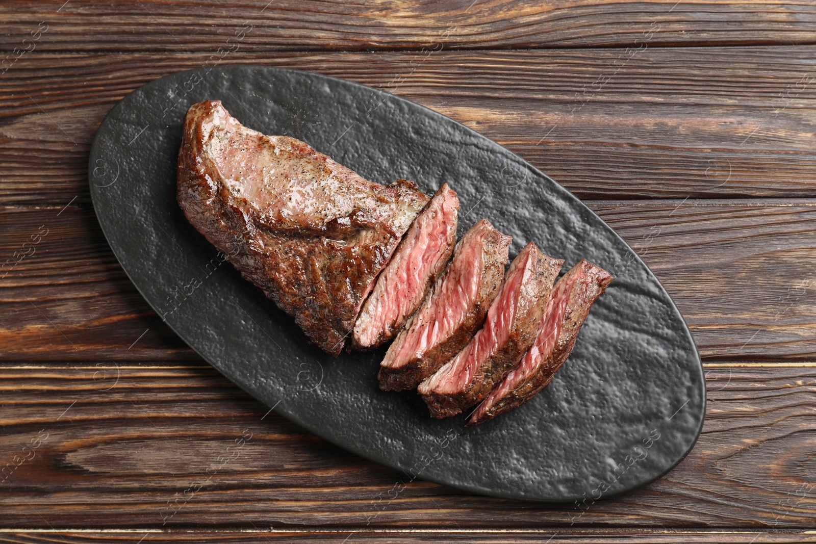 Photo of Pieces of delicious grilled beef meat on wooden table, top view