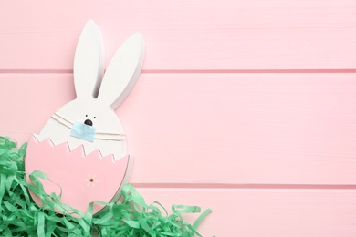 Photo of Cute bunny figure in protective mask on pink wooden background, top view with space for text. Easter holiday during COVID-19 quarantine