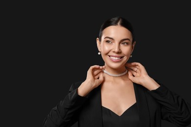 Young woman with elegant pearl jewelry on black background, space for text