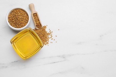 Photo of Natural oil and mustard seeds on white marble table, flat lay. Space for text