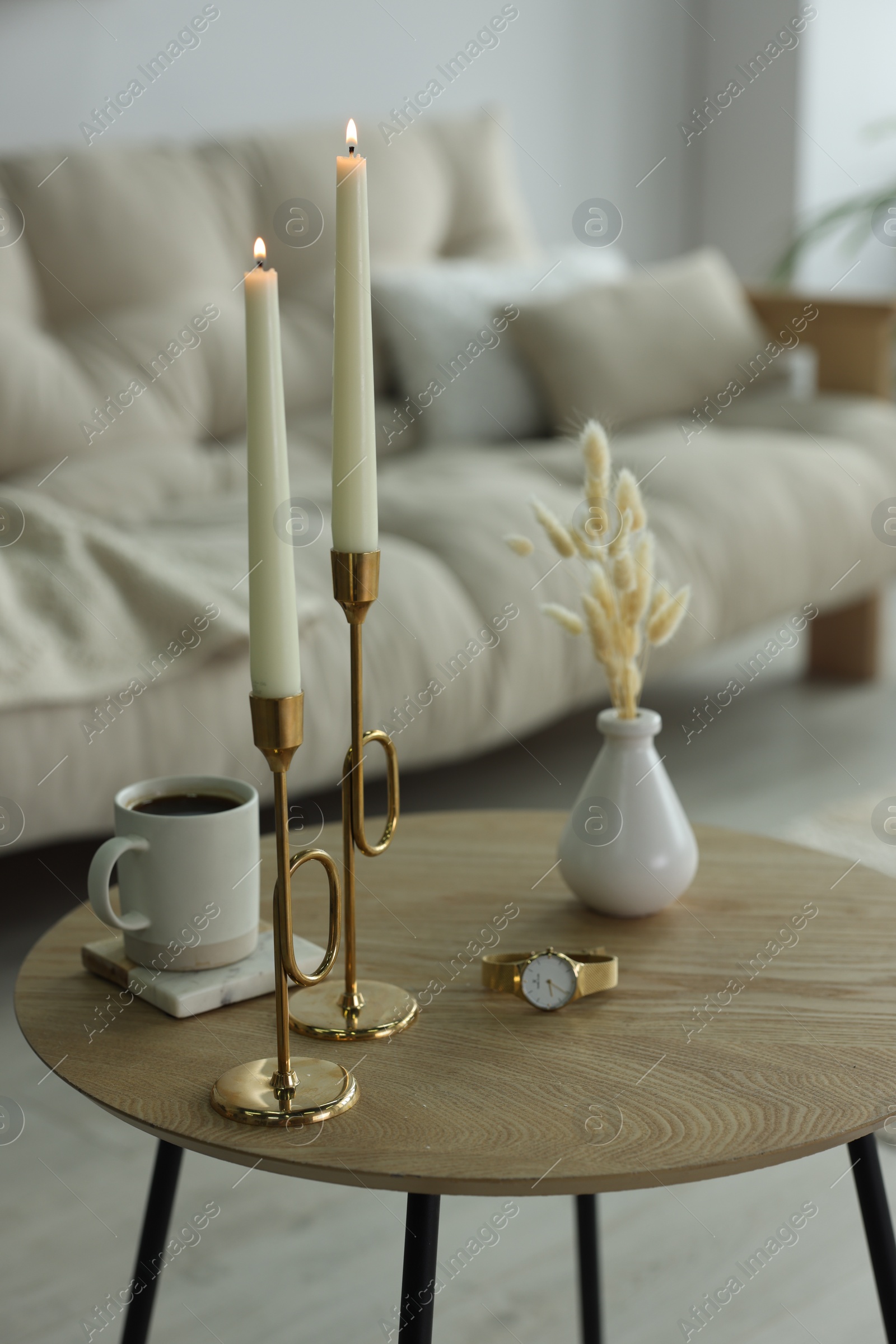 Photo of Burning candles, vase, cup of hot drink and wristwatch on wooden table in living room