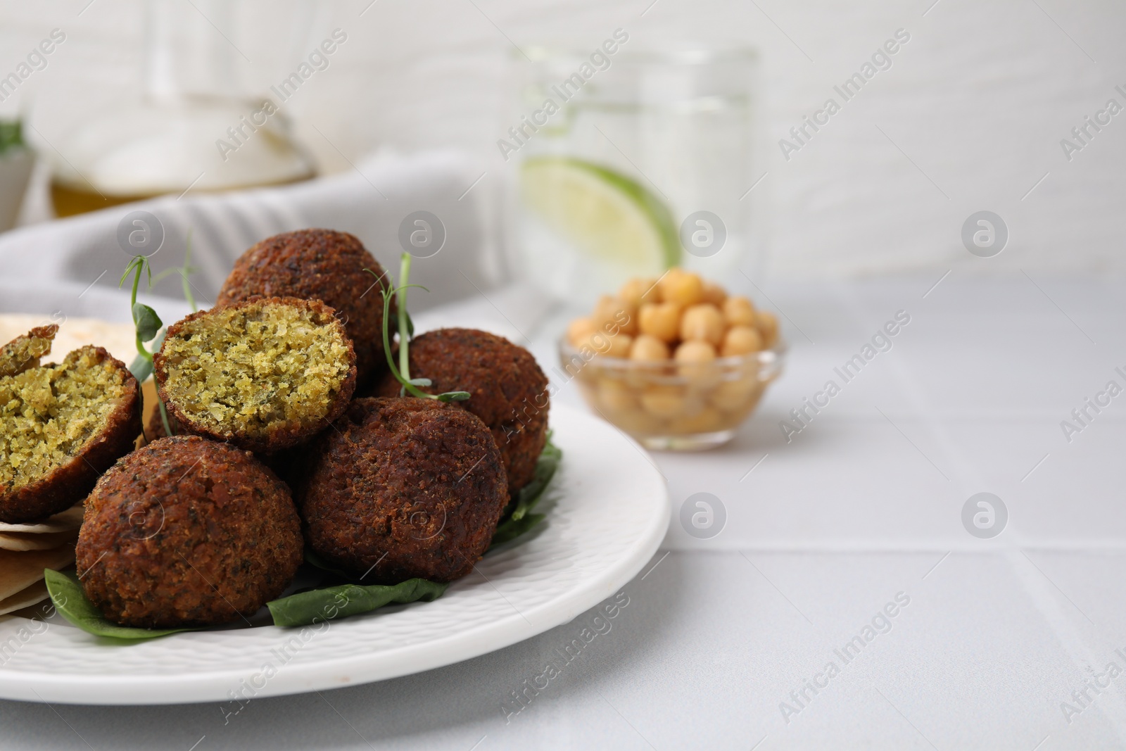 Photo of Delicious falafel balls and herbs on white tiled table, closeup. Space for text