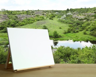 Wooden easel with blank canvas on table and beautiful view of rocky hill. Space for text