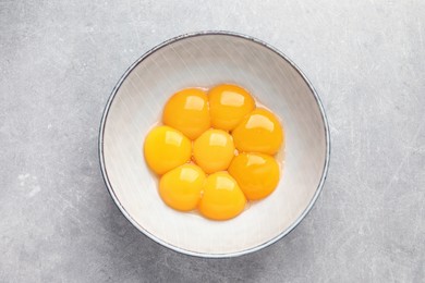 Bowl with raw egg yolks on grey table, top view