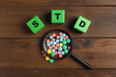 Photo of Abbreviation STD made with cubes near magnifying glass and pills on wooden table, flat lay