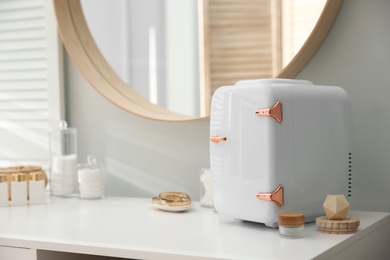 Photo of Cosmetics refrigerator and skin care products on white vanity table indoors