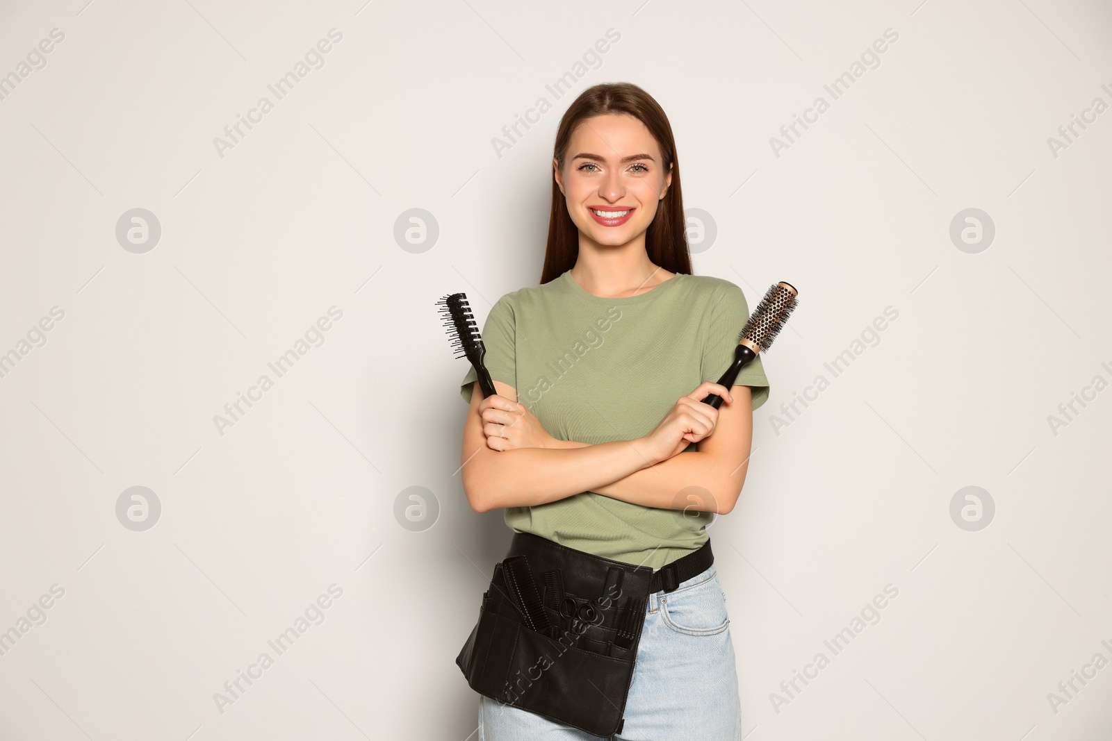 Photo of Portrait of happy hairdresser with brushes on light background