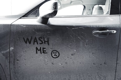 Inscription WASH ME and sad smiley on car door, closeup