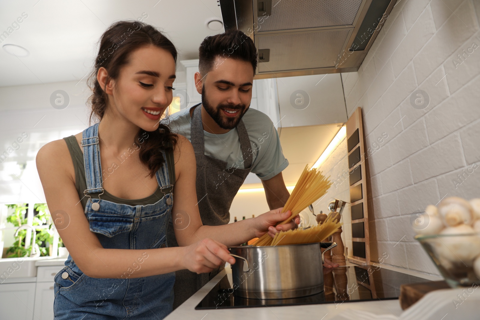 Photo of Lovely young couple cooking pasta together in kitchen