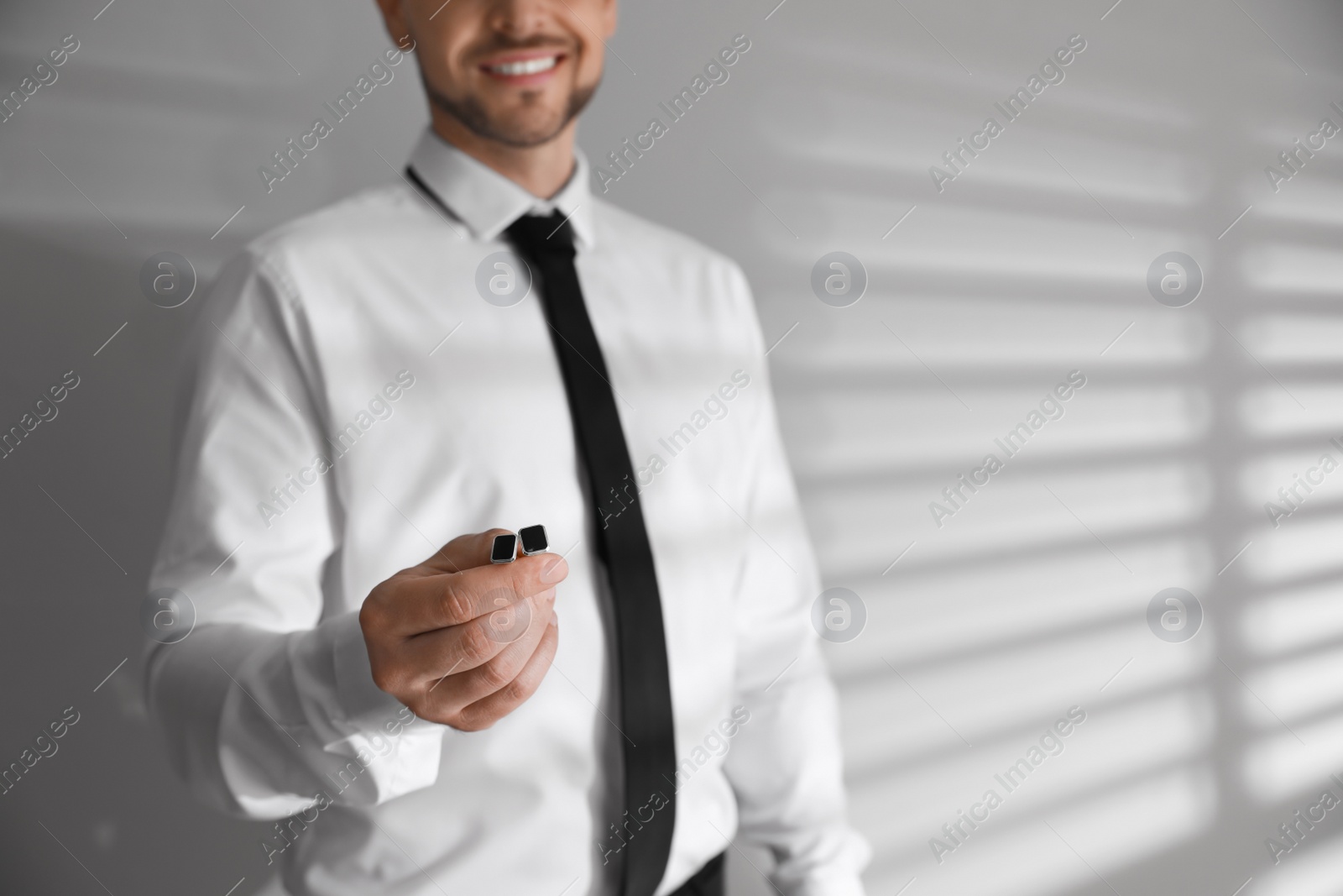 Photo of Man in shirt holding stylish cufflinks near white wall, closeup. Space for text