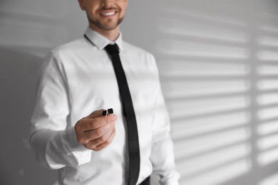 Photo of Man in shirt holding stylish cufflinks near white wall, closeup. Space for text