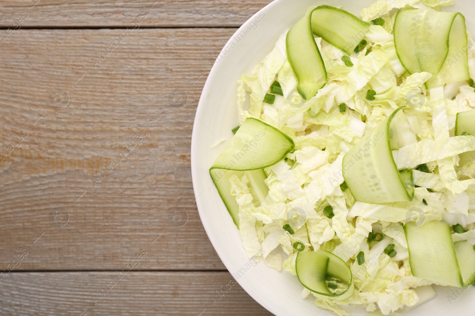 Photo of Tasty salad with Chinese cabbage, cucumber and green onion in bowl on wooden table, top view. Space for text