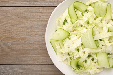 Photo of Tasty salad with Chinese cabbage, cucumber and green onion in bowl on wooden table, top view. Space for text