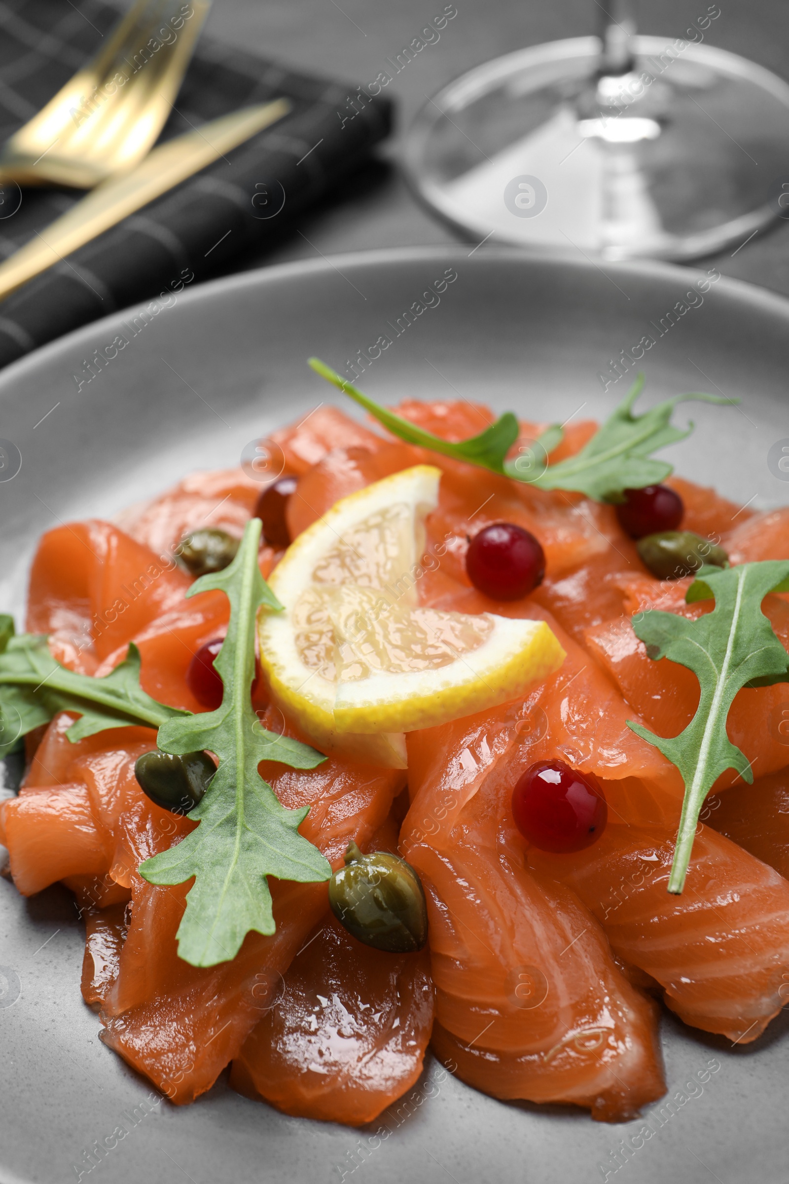 Photo of Salmon carpaccio with capers, cranberries, arugula and lemon on plate, closeup