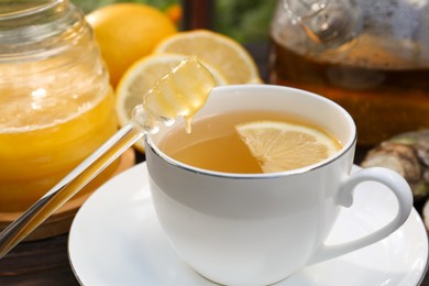 Cup of delicious tea with lemon and honey on wooden table, closeup