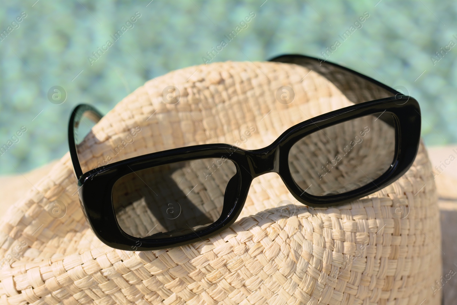 Photo of Stylish hat and sunglasses near outdoor swimming pool on sunny day, closeup