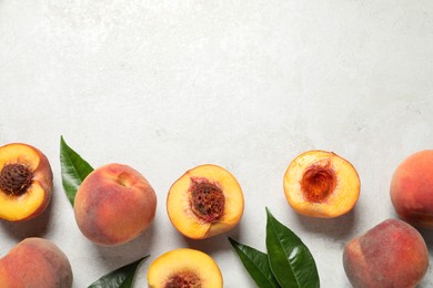 Delicious juicy ripe peaches and leaves on light grey textured table, flat lay. Space for text
