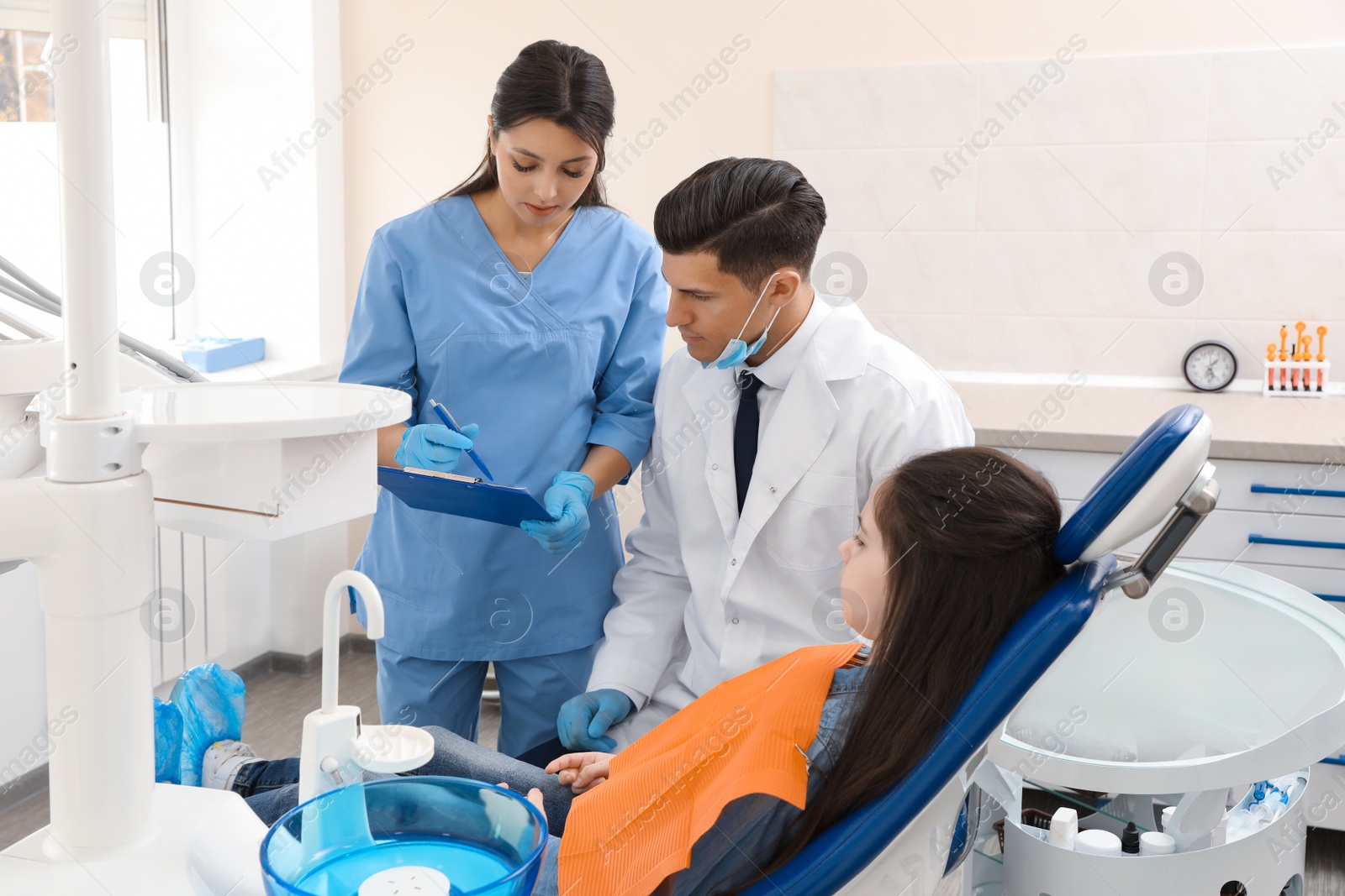 Photo of Professional dentist and assistant working with little girl in clinic