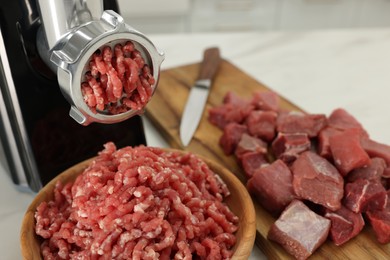 Photo of Electric meat grinder with beef on white table indoors