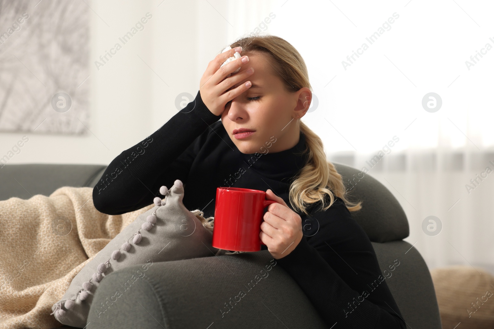 Photo of Sick woman with tissue and cup of drink on sofa at home. Cold symptoms