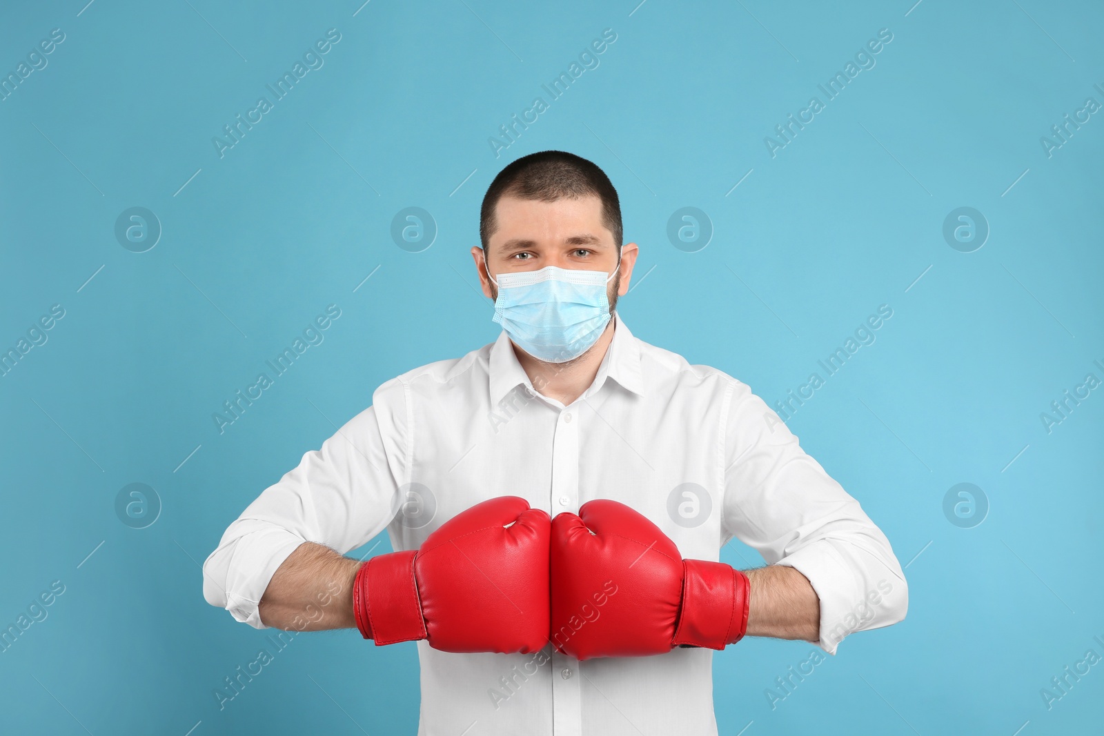 Photo of Man with protective mask and boxing gloves on light blue background. Strong immunity concept