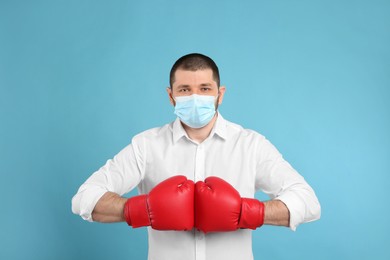 Man with protective mask and boxing gloves on light blue background. Strong immunity concept