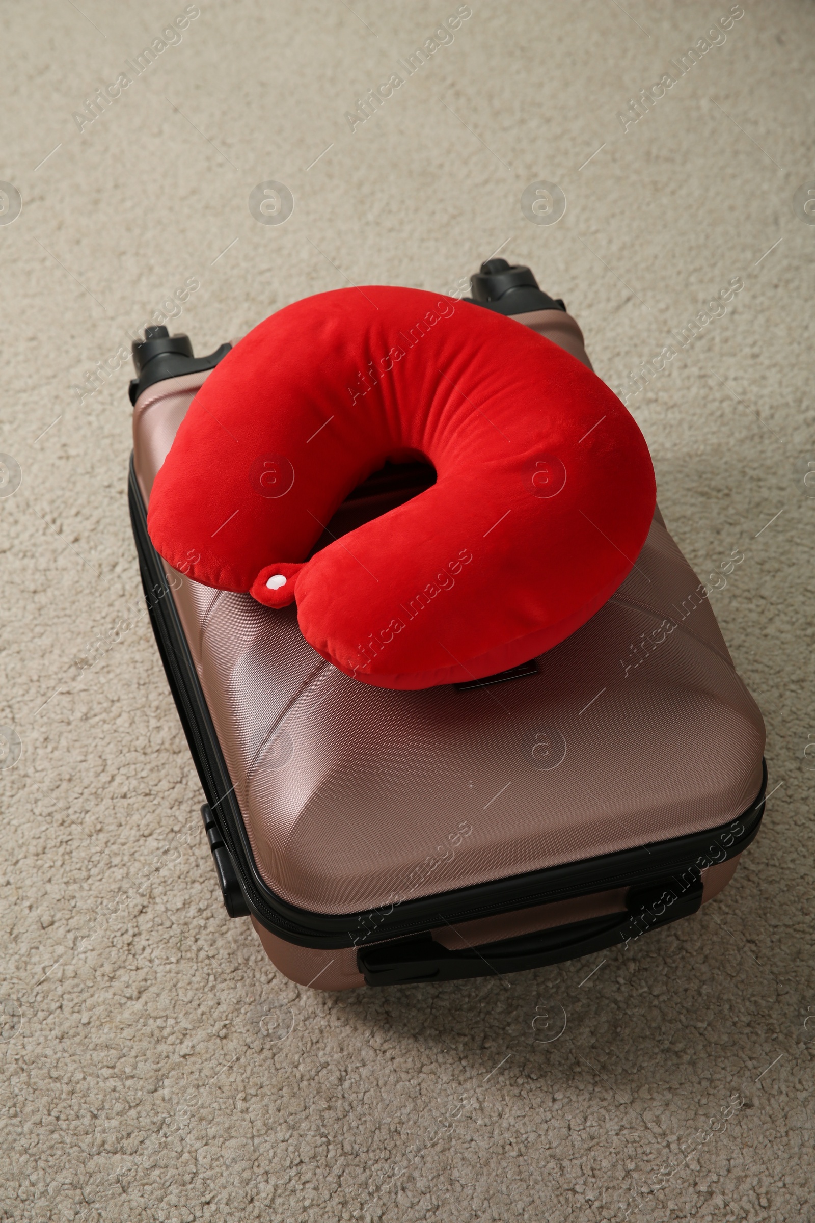 Photo of Red travel pillow and suitcase on beige rug