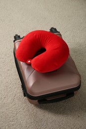 Photo of Red travel pillow and suitcase on beige rug