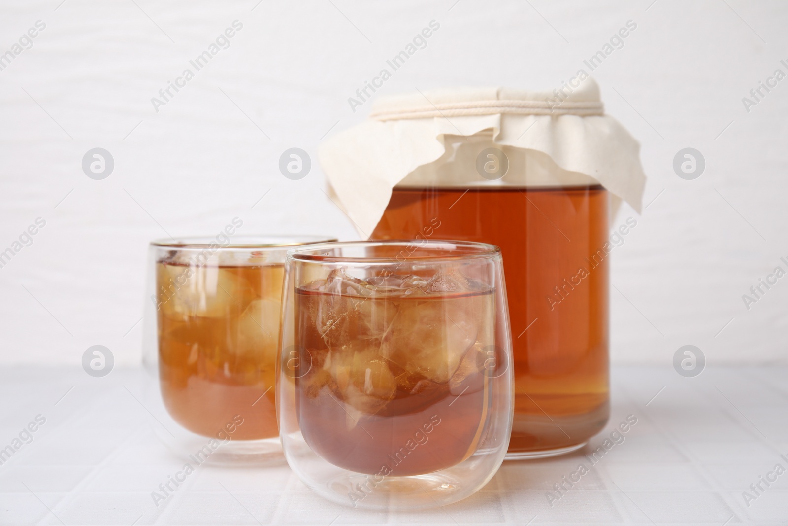 Photo of Tasty kombucha with ice cubes on white tiled table