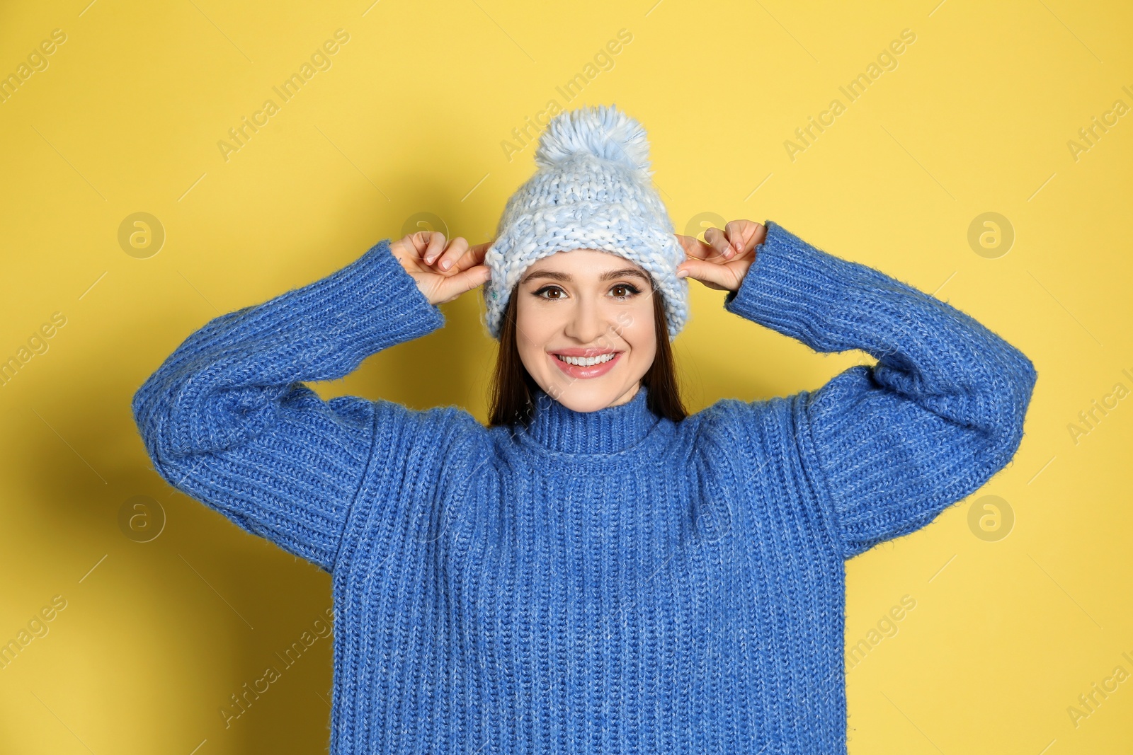 Photo of Young woman wearing warm sweater and hat on yellow background. Winter season