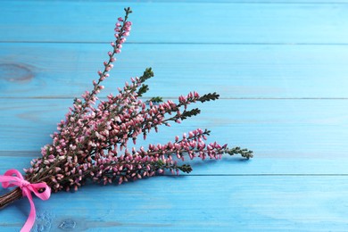 Bunch of heather branches with beautiful flowers and ribbon on light blue wooden table, space for text