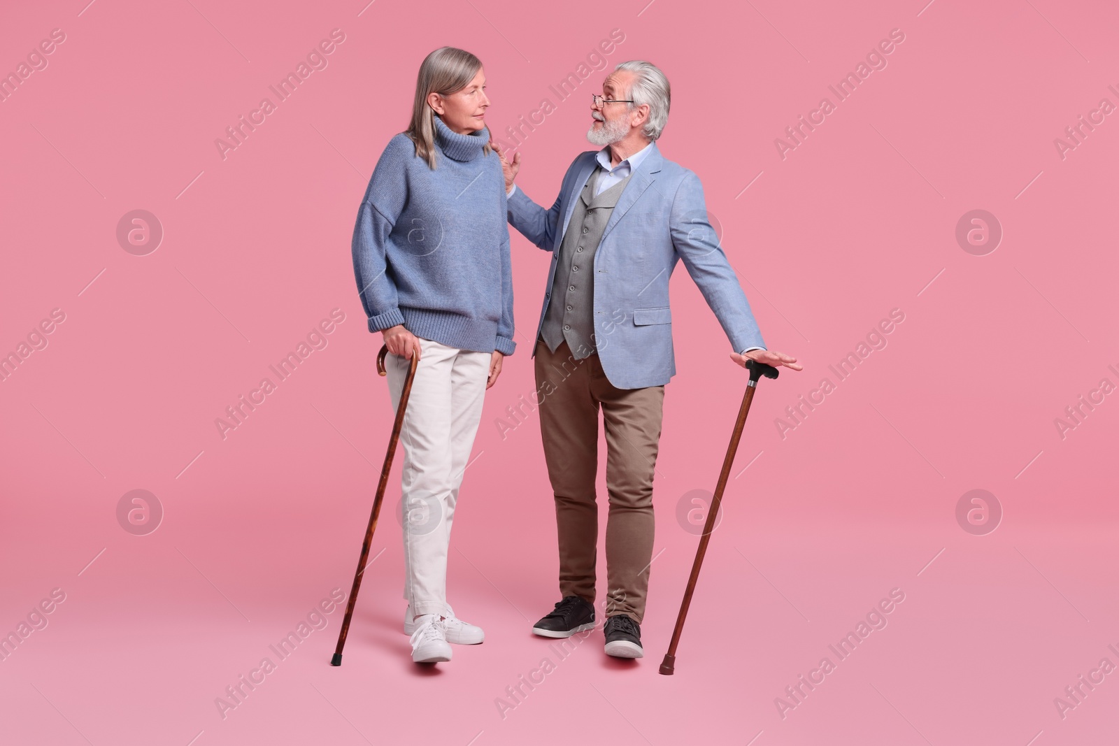 Photo of Senior man and woman with walking canes on pink background