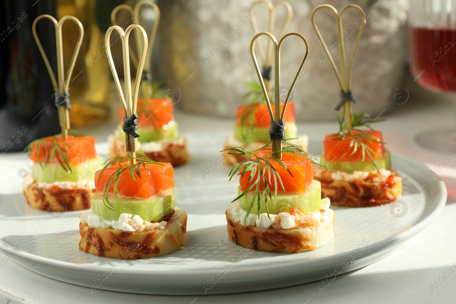 Photo of Tasty canapes with salmon, cucumber, bread and cream cheese on white table, closeup