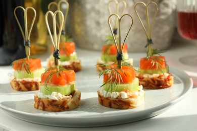 Photo of Tasty canapes with salmon, cucumber, bread and cream cheese on white table, closeup