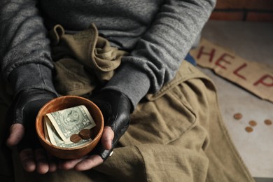 Photo of Poor homeless man holding bowl with donations on floor, closeup