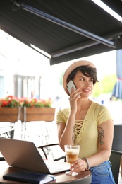 Photo of Young woman talking on phone while working with laptop at desk in cafe