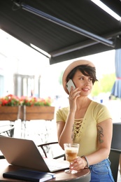 Young woman talking on phone while working with laptop at desk in cafe