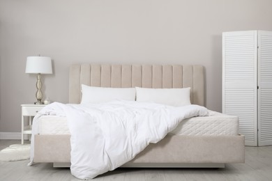 Comfortable bed with soft white mattress, blanket and pillows indoors