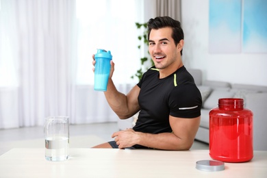 Photo of Young athletic man with protein shake at home, space for text