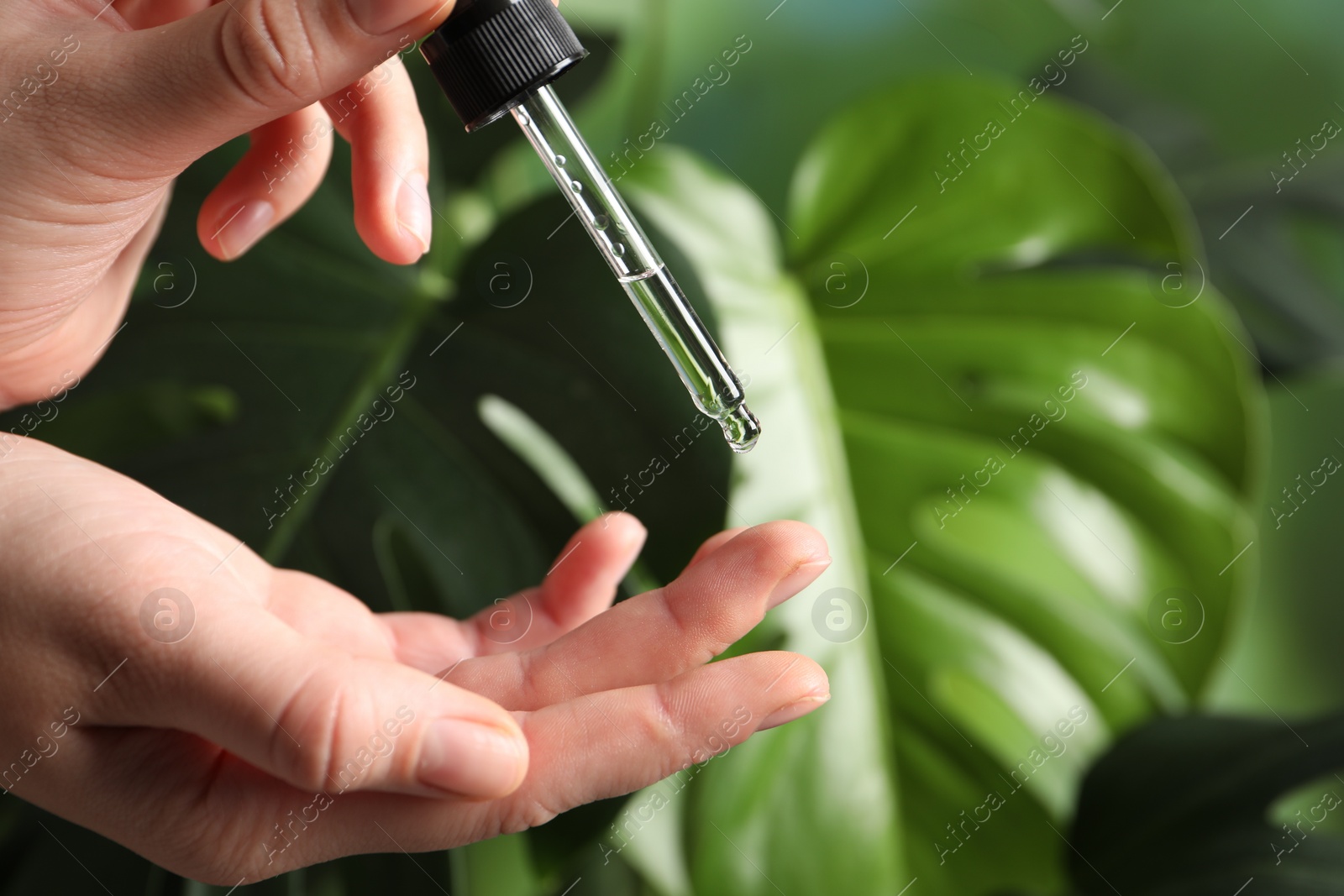 Photo of Woman applying cosmetic serum onto finger on blurred background, closeup. Space for text