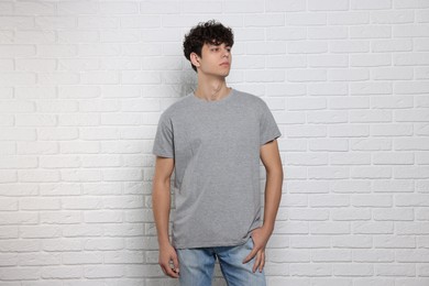 Photo of Man wearing gray t-shirt near white brick wall. Mockup for design