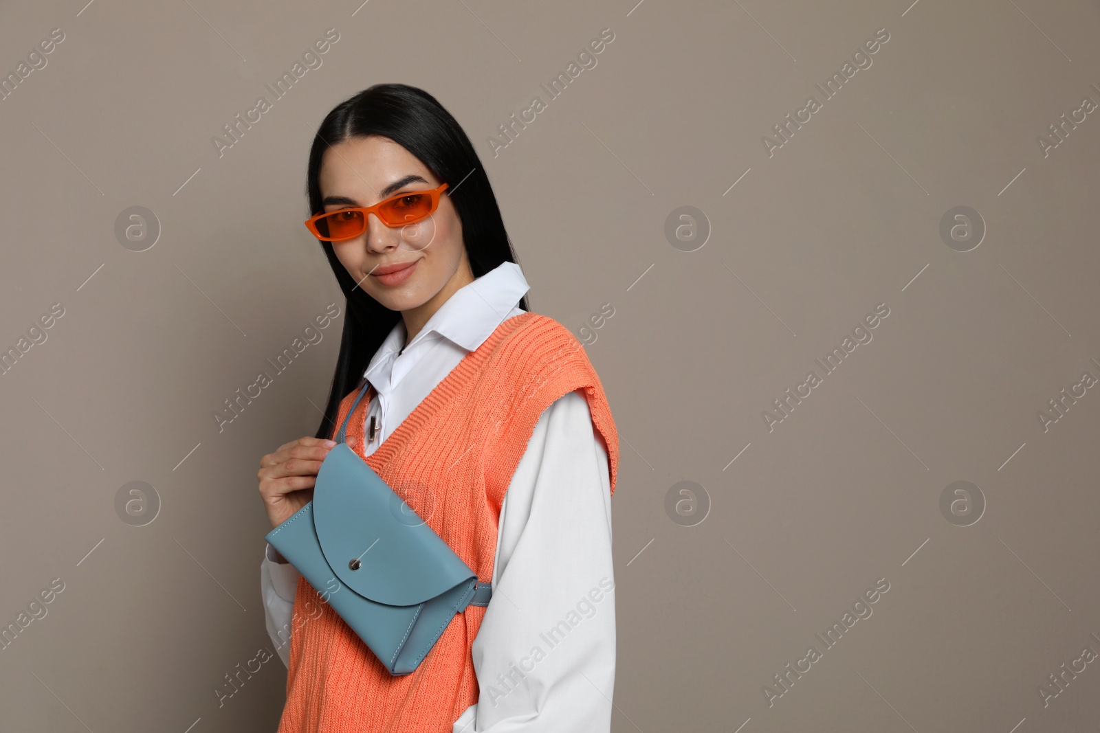 Photo of Beautiful young woman with stylish waist bag on grey background, space for text