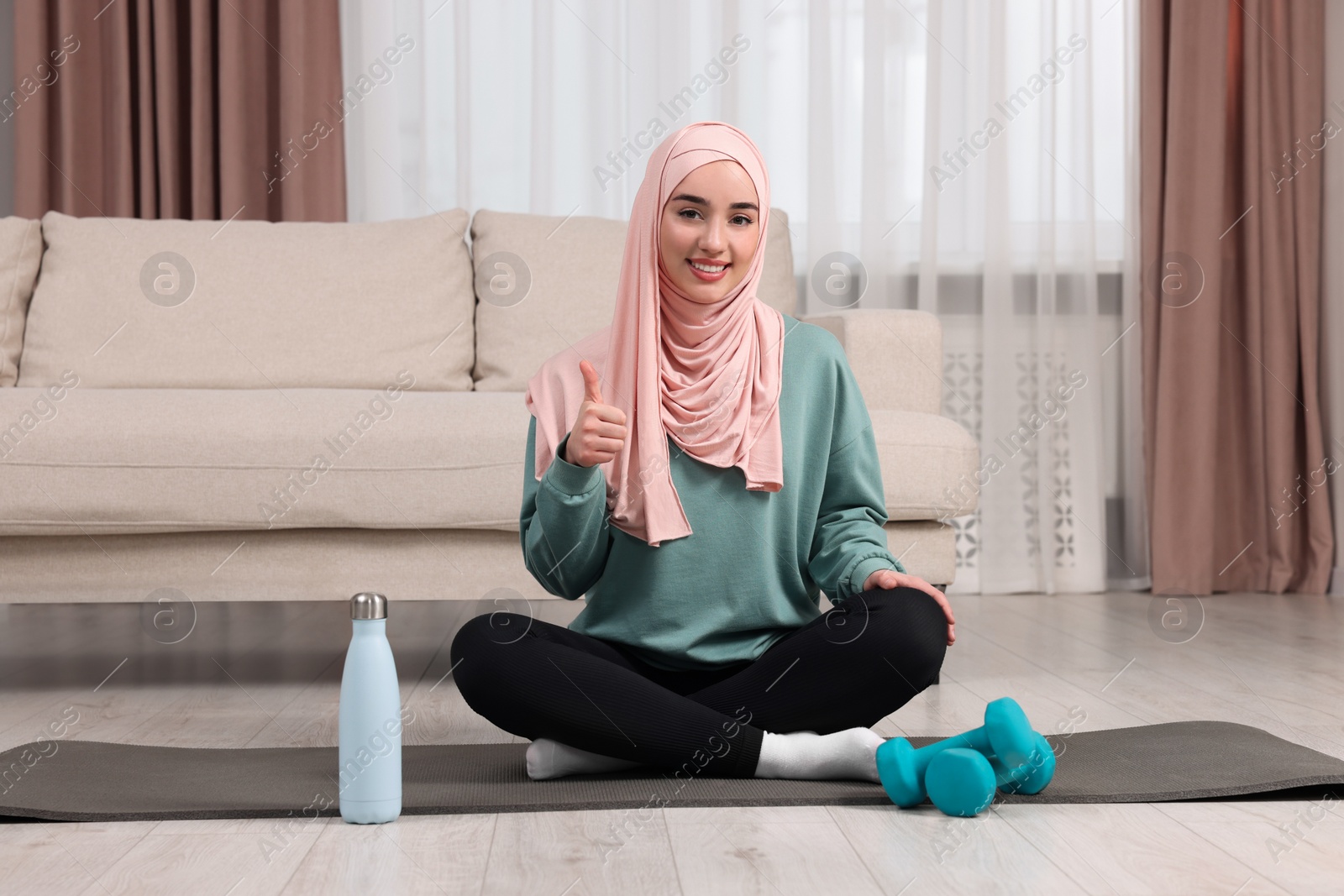 Photo of Muslim woman showing thumb up on fitness mat at home