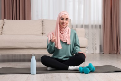 Photo of Muslim woman showing thumb up on fitness mat at home