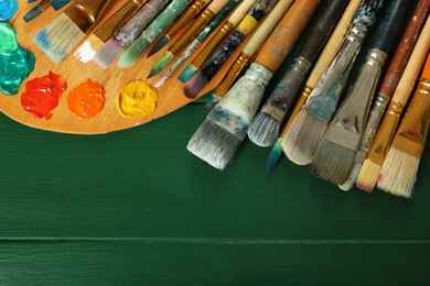 Photo of Many paintbrushes and palette on green wooden table, flat lay. Space for text