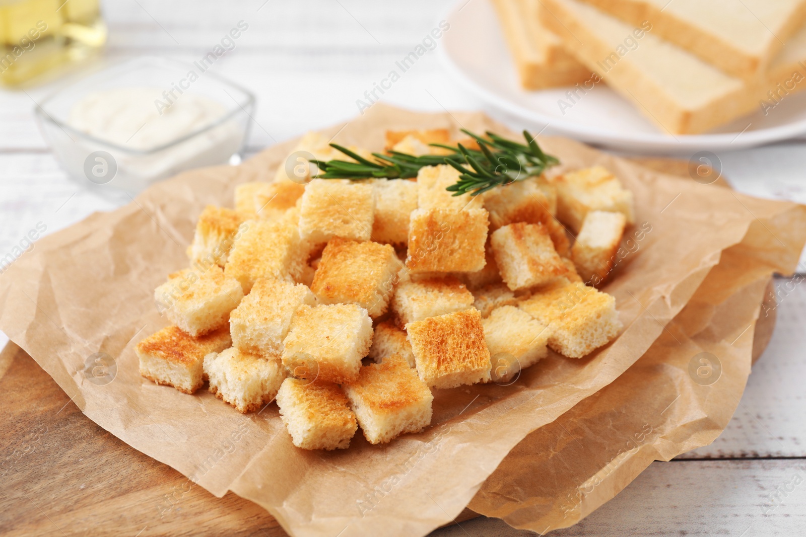 Photo of Delicious crispy croutons with rosemary on white wooden board, closeup