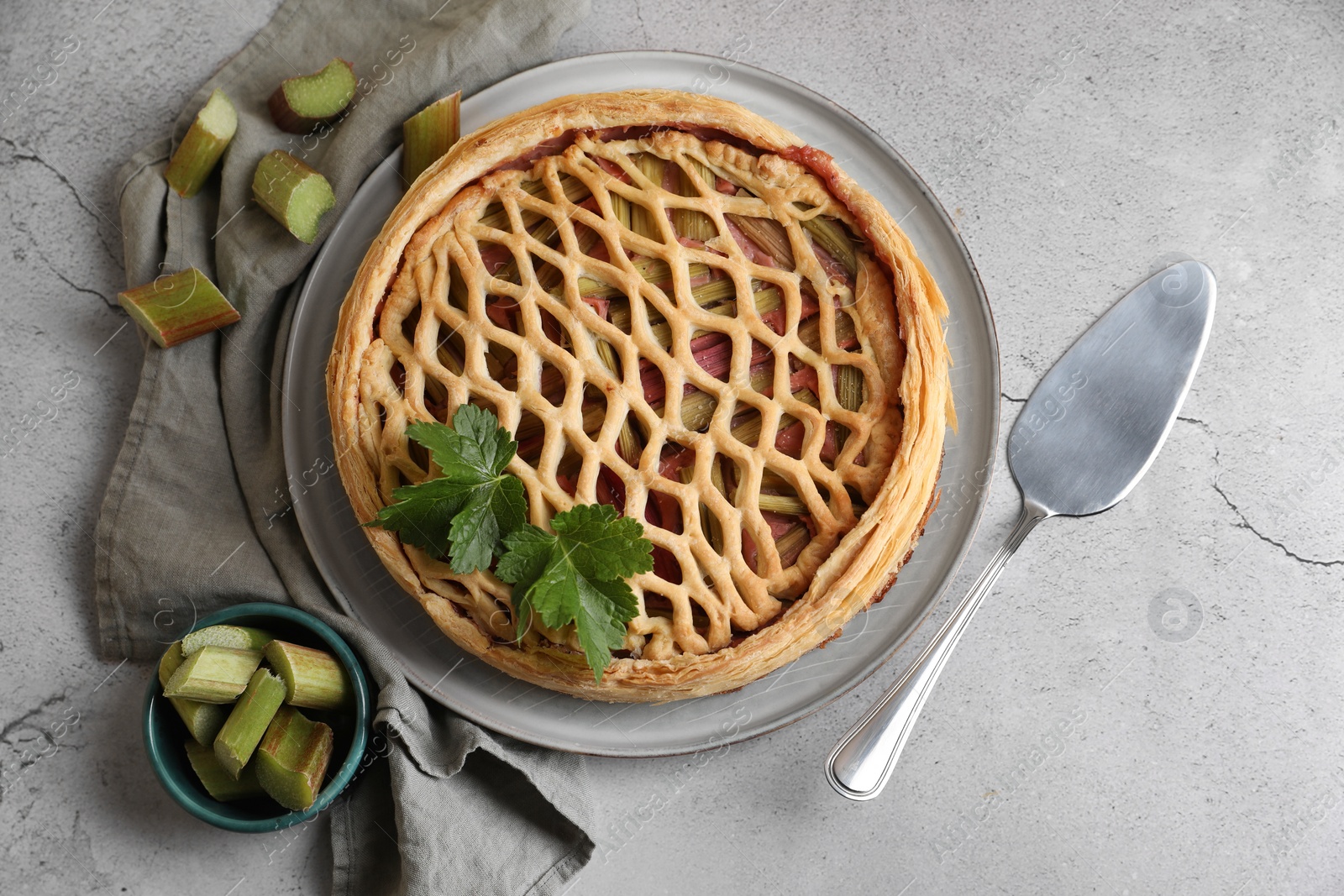 Photo of Freshly baked rhubarb pie, cut stalks and cake server on light grey table, flat lay